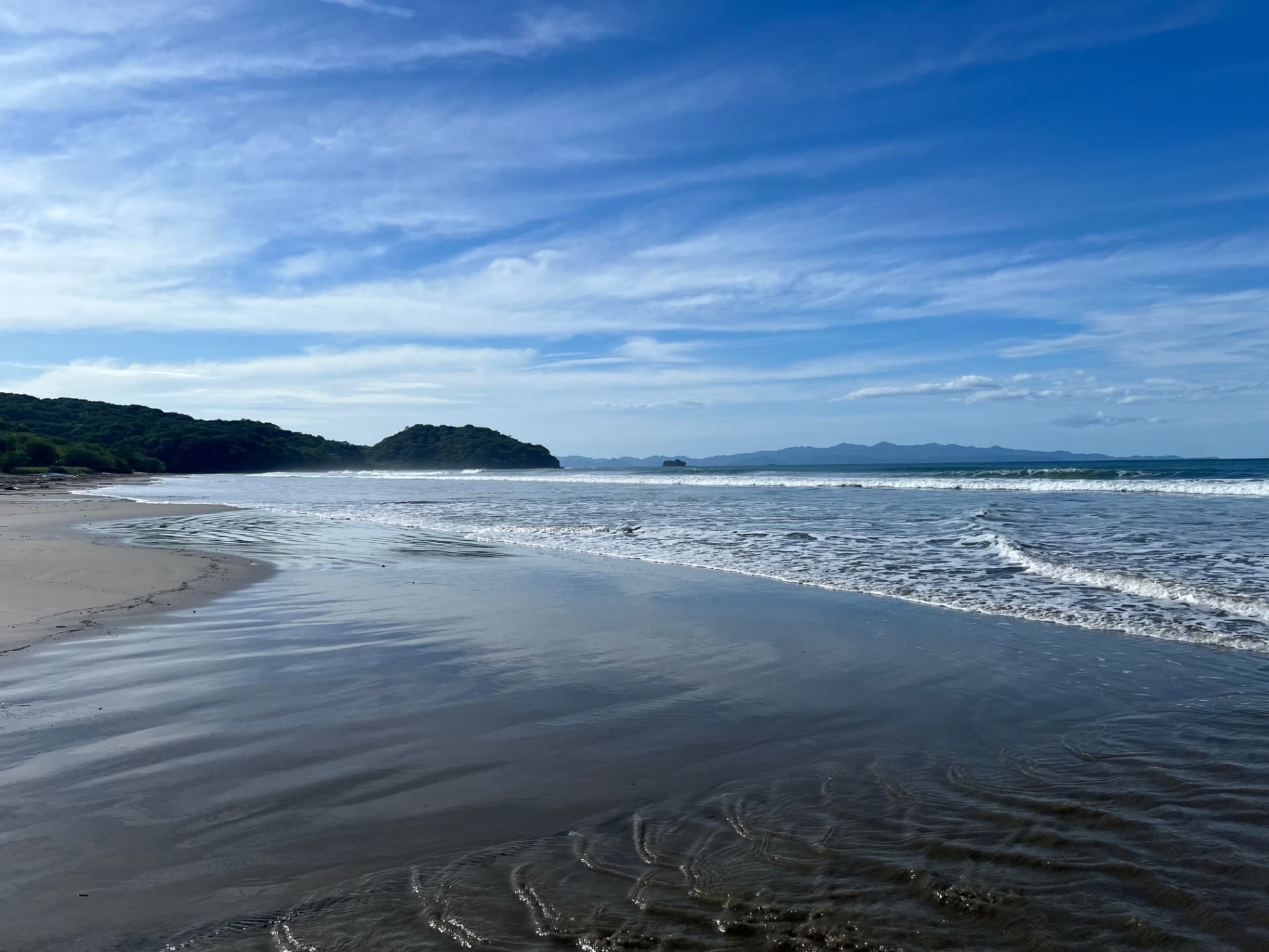 The broad shoreline, ocean and distant headlands of Playa El Coco beneath an open blue sky